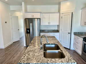 Kitchen featuring white cabinets, a center island with sink, appliances with stainless steel finishes, and dark hardwood / wood-style flooring