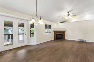 Unfurnished living room with ceiling fan with notable chandelier, lofted ceiling, hardwood / wood-style floors, and a tiled fireplace