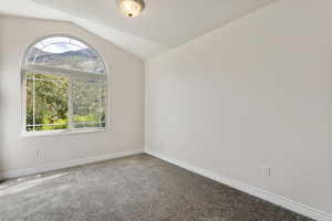 Empty room with vaulted ceiling and carpet flooring