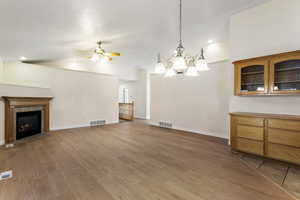 Unfurnished living room with ceiling fan with notable chandelier, light wood-type flooring, vaulted ceiling, and a fireplace