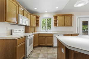 Kitchen featuring white appliances, light tile patterned flooring, sink, and kitchen peninsula