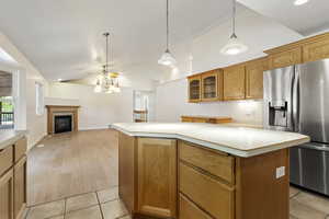 Kitchen featuring light wood-type flooring, stainless steel fridge with ice dispenser, lofted ceiling, a kitchen island, and decorative light fixtures