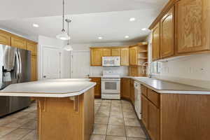 Kitchen with a center island, sink, white appliances, light tile patterned floors, and decorative light fixtures