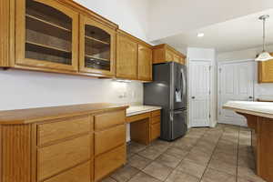 Kitchen with pendant lighting, light tile patterned flooring, built in desk, and stainless steel fridge with ice dispenser