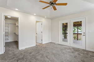 Unfurnished bedroom featuring a spacious closet, a closet, ceiling fan, access to outside, and light colored carpet