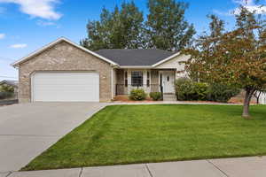 Ranch-style house featuring a garage, a front lawn, and covered porch