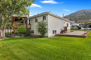 Back of property with a deck with mountain view, a patio, and a lawn