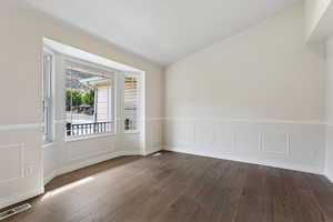 Empty room with vaulted ceiling and dark hardwood / wood-style flooring