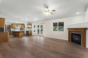 Unfurnished living room featuring a tile fireplace, ceiling fan with notable chandelier, vaulted ceiling, and dark hardwood / wood-style floors