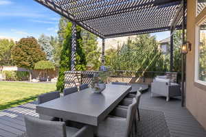 Outdoor dining area on rear deck w/ large wooden trellis above, overlooking matured landscaped backyard.