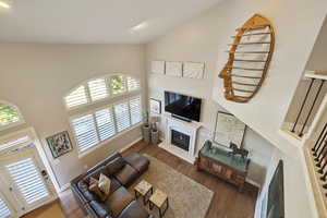 View from upstairs loft space looking onto living room w/ hardwood flooring, double height vaulted ceilings & recessed lighting.