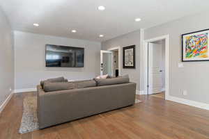 Basement family room w/ hardwood flooring, recessed lighting & view of wine vault room.