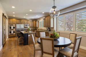 View of open semi formal dining area w/ recessed lighting, large glass globe pendant fixture, hardwood flooring & custom wood & iron pantry barn door.