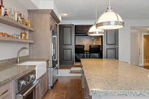 Well-appointed 2nd full kitchen, large granite topped island, custom pendant light fixtures & home theater in background.