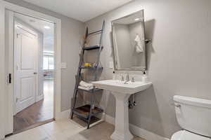 Bathroom w/ pedestal sink, custom pivoting metal framed mirror, tile flooring & recessed lighting.