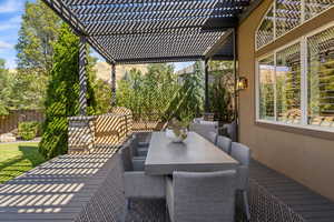 View of wooden deck featuring an outdoor dining area & wooden trellis overlooking private backyard.