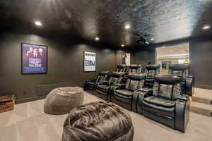 Theater room w/ light carpet flooring, recessed lighting, tiered seating platforms & powered leather reclining chairs.