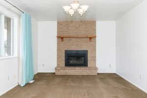 Unfurnished living room featuring a fireplace, carpet flooring, and an inviting chandelier