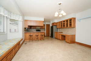 Kitchen featuring pendant lighting, stainless steel fridge, backsplash, a chandelier, and a kitchen breakfast bar