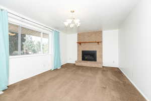 Unfurnished living room with carpet floors, an inviting chandelier, and a brick fireplace