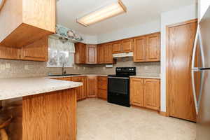 Kitchen with black electric range, sink, kitchen peninsula, and tasteful backsplash