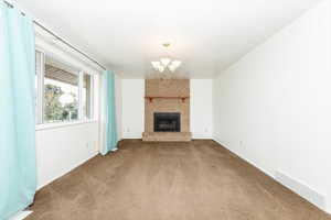 Unfurnished living room featuring a fireplace, a chandelier, and carpet