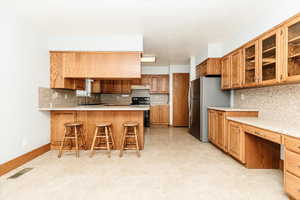 Kitchen featuring sink, a breakfast bar area, kitchen peninsula, stainless steel refrigerator, and backsplash