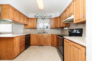 Kitchen with sink, kitchen peninsula, backsplash, black appliances, and light tile patterned floors