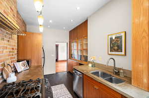 Kitchen with pendant lighting, dark hardwood / wood-style floors, sink, stainless steel appliances, and brick wall