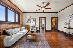 Living room featuring crown molding, dark hardwood / wood-style floors, ceiling fan, and brick wall