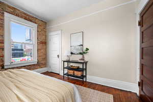 Bedroom featuring brick wall and dark hardwood / wood-style flooring