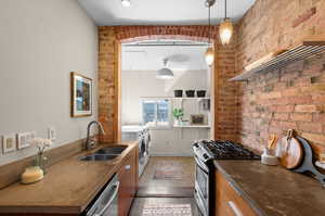 Kitchen with sink, hanging light fixtures, appliances with stainless steel finishes, independent washer and dryer, and brick wall