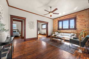 Living room with a wealth of natural light, ceiling fan, brick wall, and dark wood-type flooring