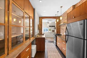 Kitchen with appliances with stainless steel finishes, dark hardwood / wood-style floors, pendant lighting, and brick wall