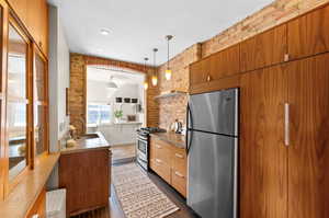 Kitchen featuring brick wall, dark hardwood / wood-style flooring, pendant lighting, stainless steel appliances, and sink