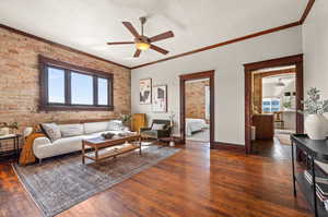 Living room featuring dark wood-type flooring, ceiling fan, and brick wall