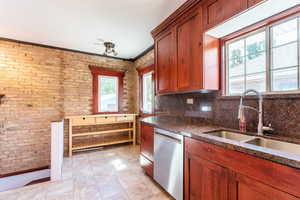 Kitchen with ornamental molding, sink, stainless steel dishwasher, brick wall, and decorative backsplash