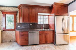 Kitchen featuring sink, tasteful backsplash, brick wall, stainless steel appliances, and dark stone countertops