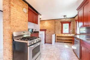 Kitchen featuring brick wall, appliances with stainless steel finishes, and light tile patterned floors