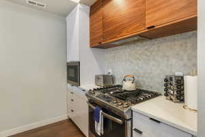 Kitchen featuring white cabinets, stainless steel range with gas cooktop, dark hardwood / wood-style flooring, and black microwave