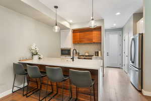 Kitchen featuring appliances with stainless steel finishes, white cabinets, kitchen peninsula, pendant lighting, and light wood-type flooring