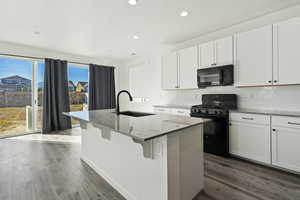 Kitchen featuring white cabinets, black appliances, a kitchen island with sink, and sink