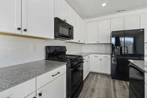 Kitchen with decorative backsplash, dark wood-type flooring, light stone counters, white cabinets, and black appliances