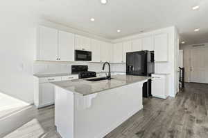 Kitchen with white cabinets, an island with sink, sink, black appliances, and hardwood / wood-style floors