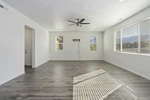 Empty room featuring ceiling fan, dark hardwood / wood-style floors, a healthy amount of sunlight, and a textured ceiling