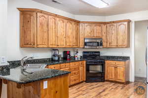 Kitchen featuring light wood-type flooring, a textured ceiling, sink, kitchen peninsula, and black range with gas cooktop