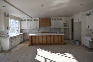 Kitchen featuring sink, a spacious island, white cabinets, premium range hood, and decorative backsplash