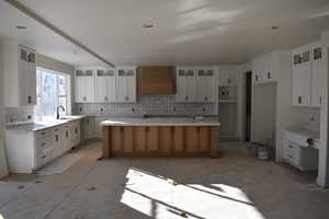 Kitchen with white cabinets, sink, tasteful backsplash, custom exhaust hood, and a spacious island