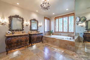 Bathroom featuring a notable chandelier, tiled tub, and vanity