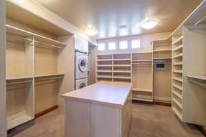 Walk in closet with light colored carpet and stacked washing maching and dryer